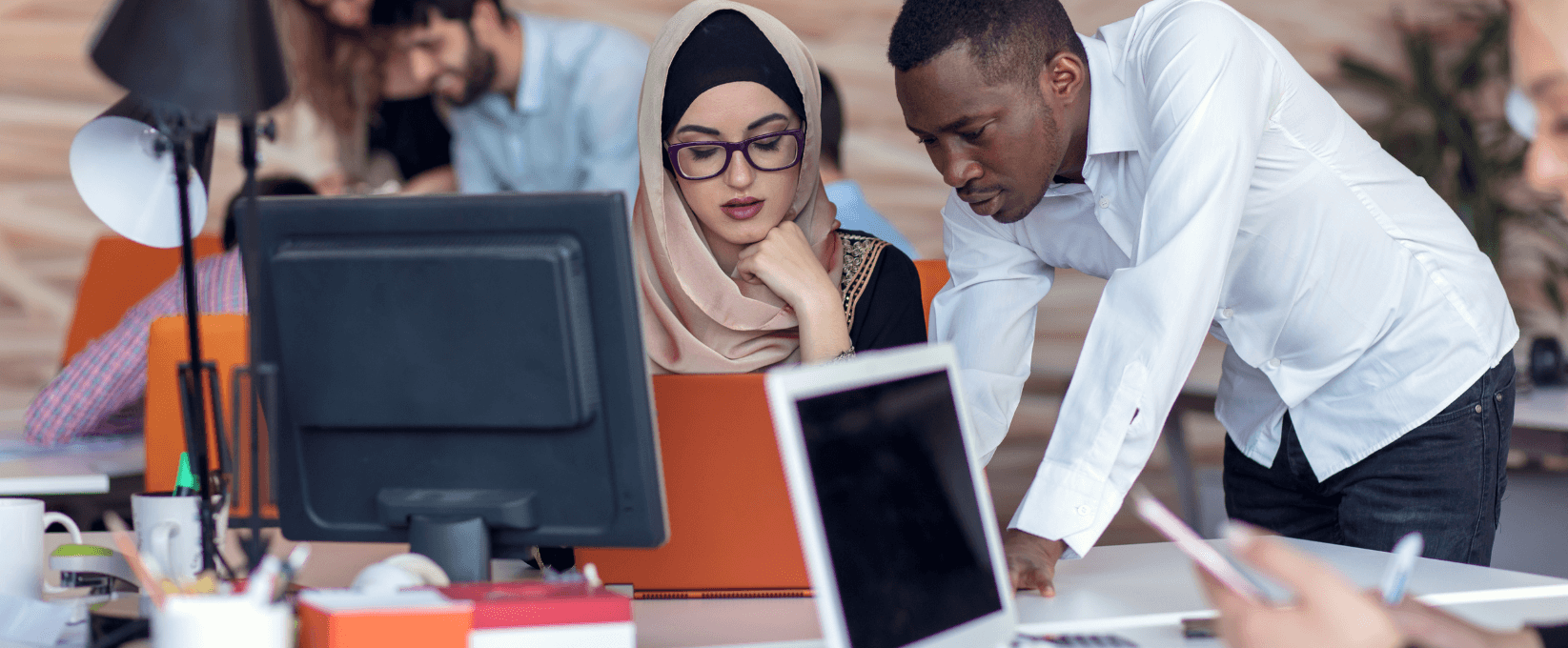 A Black man and a Muslim woman working together looking at a computer.